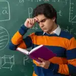 Student holding a book and scratching head in front of a chalkboard while studying SAT Math